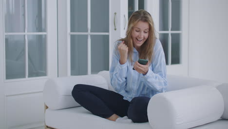 Funny-euphoric-young-woman-customer-celebrating-winning-bid-or-getting-ecommerce-shopping-offer-on-smartphone.-Excited-girl-winner-looking-at-mobile-phone-using-app-celebrating-success-concept.